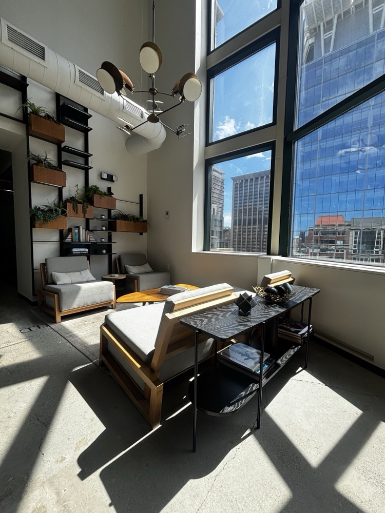A seating area beneath tall black-framed windows, with planted shelving running up the wall.