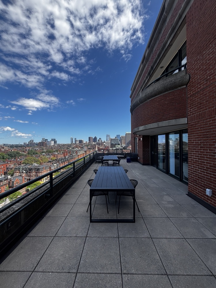 A long table running the length of the terrace toward the Boston skyline, with the building's brick facade alongside.
